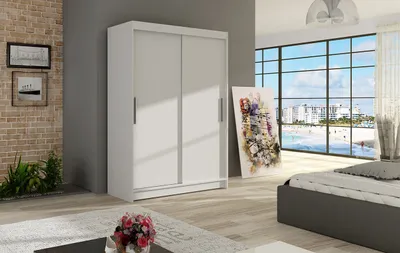 A modern bedroom with a white sliding door wardrobe, a bed, and a large window overlooking a beach.