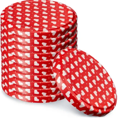 A stack of red jar lids with white heart patterns and a single lid placed in front of the stack.