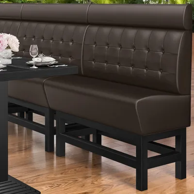 A dark brown leather Chesterfield button high bench with a black metal frame, set against a blurred background of greenery and a wooden floor.