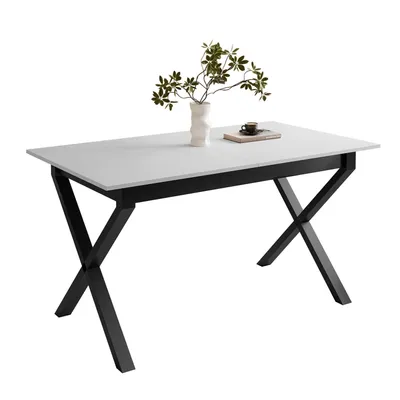 A white dining table with black X-shaped legs, a vase with green branches, and a book with a cup on it.