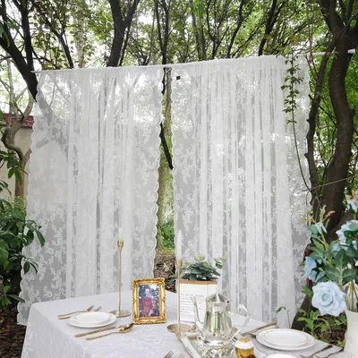 A table setting with white lace curtains in the background, outdoors among trees.