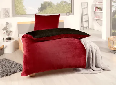 A bedroom scene with a bed made up with red and black bedding, a gray blanket, and a rug.