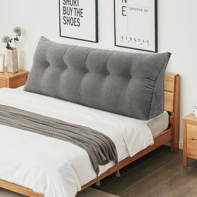 A grey wedge pillow is placed on a bed with white sheets and a grey throw blanket.