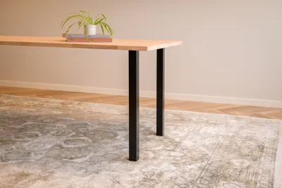 A close-up shot of a wooden table with black metal legs, placed on a patterned rug.