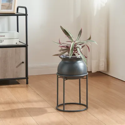 A plant in a pot on a stand next to a shelf unit.