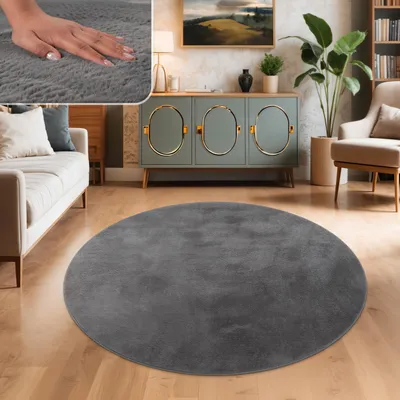 A circular gray rug is placed on a wooden floor in a living room setting, with a sofa and a cabinet in the background.