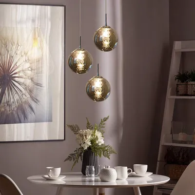 A dining table set with cups and a vase of flowers, under three pendant lights.
