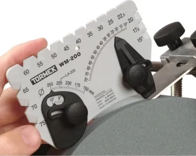 A hand is holding a Tormek WM-200 angle gauge against a grinding wheel.