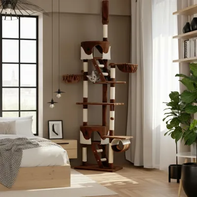A cat tree is set up in a bedroom next to a bed and a window.
