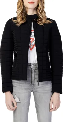 A woman is wearing a black quilted jacket over a white t-shirt and grey jeans.