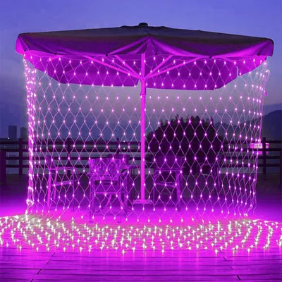 A patio umbrella decorated with pink net lights at dusk.
