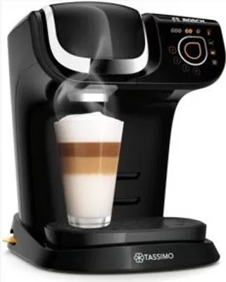 A black Tassimo coffee machine brewing a layered latte into a clear glass.