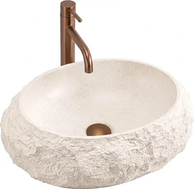 A beige stone-like vessel sink with a bronze faucet.