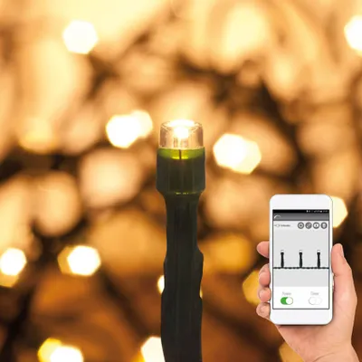 A hand holds a smartphone displaying a control interface, next to a close-up of a warm white LED light on a string of lights, with a blurred background of more lights.