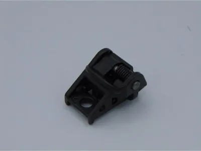 A black plastic part with a spring mechanism, likely a component for a power tool, is shown against a plain light gray background.