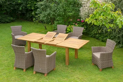 A wooden dining set with chairs is arranged on a green lawn in a garden setting.