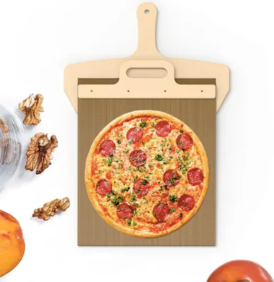 A pizza peel with a pizza on it, surrounded by walnuts and a piece of fruit.