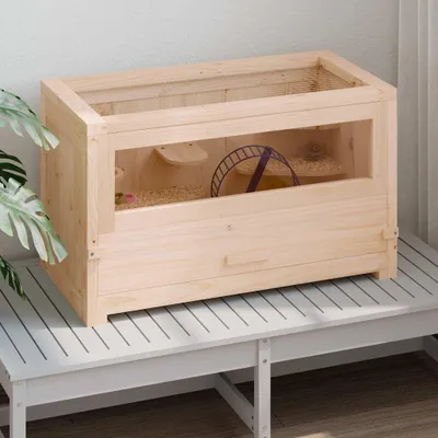 A wooden hamster cage with a wheel and bedding sits on a slatted white bench.