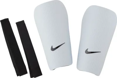A pair of white Nike shin guards with black Nike swoosh logos and two black elastic straps are laid out on a white background.