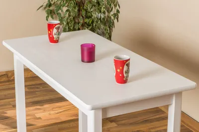 A white table with two red mugs and a purple candle on it, with a plant in the background.