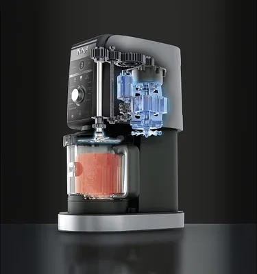 A cutaway view of a Ninja Creami ice cream maker, showing its internal mechanisms and a container filled with a pink mixture.