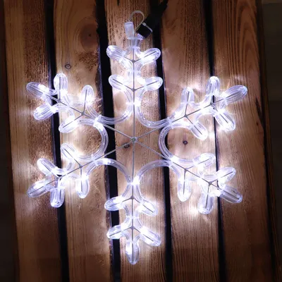 A lit snowflake decoration is placed on a wooden surface.