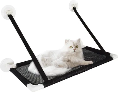 A white cat is lying on a black mesh hammock attached to a window with suction cups.