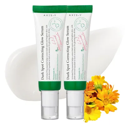Two tubes of Axis-Y Dark Spot Correcting Glow Serum are displayed prominently, with a swirl of white cream behind them and a cluster of yellow and orange flowers to the right.