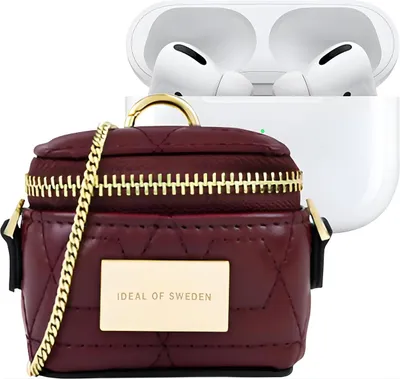 A burgundy AirPods case with a gold chain and a gold plate with the brand name, next to an open white AirPods charging case with AirPods inside.