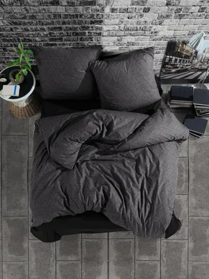 A top-down view of a bed with grey bedding and pillows, set against a brick wall.