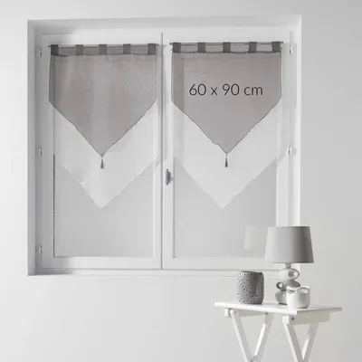 Two short curtains hanging on a window, with a table and lamp in the foreground.