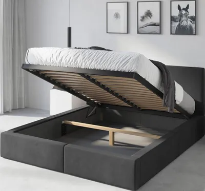 A bed with its storage compartment open, revealing the slatted base and internal space. The bed is upholstered in dark gray fabric.
