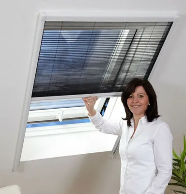 A woman is adjusting a pleated blind on a skylight window.