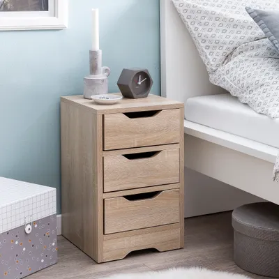 A bedside table with three drawers next to a bed.