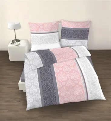 A neatly made bed with a pink, gray, and white patterned duvet and pillows, placed on a wooden floor next to a white side table with a lamp.