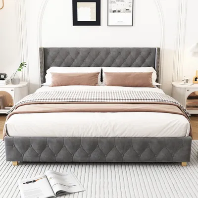 A bed with gray tufted headboard and frame, dressed with white and gray bedding, and pink accent pillows.