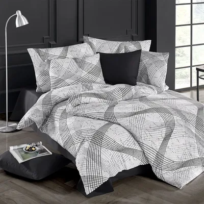 A bed with a patterned duvet and pillows, a floor lamp, and a small table with a magazine and snacks.