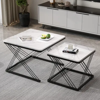 Two square coffee tables with marble-like tops and black geometric bases are placed on a gray carpet in a living room setting. A white and black media console is visible in the background, along with a potted plant.