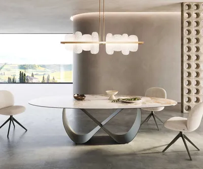 A modern dining room with an oval table and chairs, illuminated by a unique chandelier.