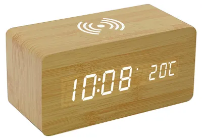 A digital alarm clock with a wood-grain finish and a wireless charging symbol on top.