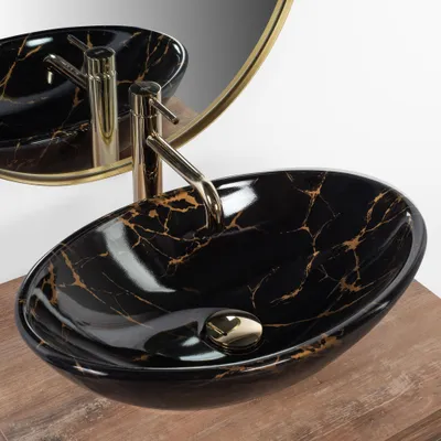 A black marble sink with gold veins and a gold faucet is shown on a wooden surface, with a gold-rimmed mirror in the background.