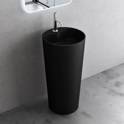 A black matte freestanding pedestal sink with a chrome faucet against a gray concrete wall.