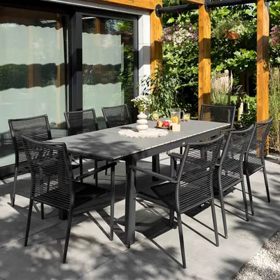 An outdoor dining set with a table and chairs on a patio, surrounded by greenery.