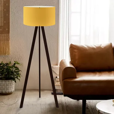 A yellow floor lamp with a tripod base stands next to a brown leather sofa in a living room.