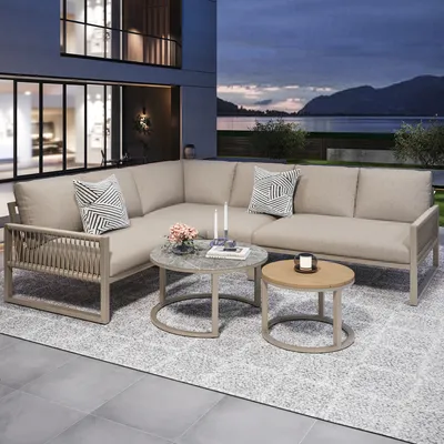 An outdoor patio setting at dusk with a sectional sofa, coffee tables, and a scenic view of a lake and mountains.