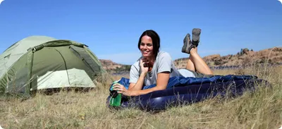 A woman is lying on an air mattress next to a tent in a grassy, outdoor environment.
