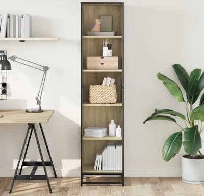 A tall, narrow bookshelf filled with various items, next to a desk and a large potted plant.