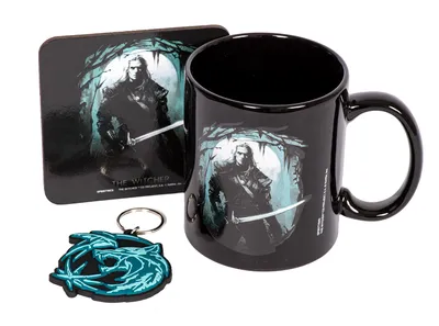 A black mug, a square coaster, and a keychain are displayed together on a white background. All items feature artwork from The Witcher, including a depiction of Geralt of Rivia and the Wolf School medallion.