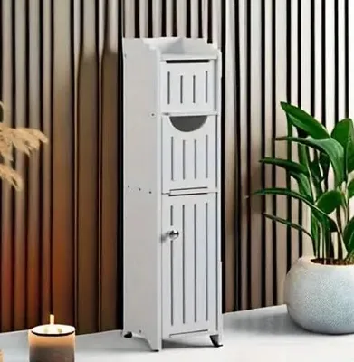 A white bathroom cabinet with drawers and a door, standing on a light-colored floor against a striped background.