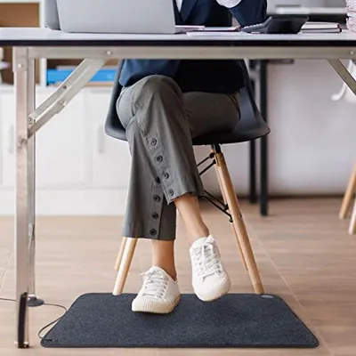 A person sitting at a desk with their feet on a heated mat.